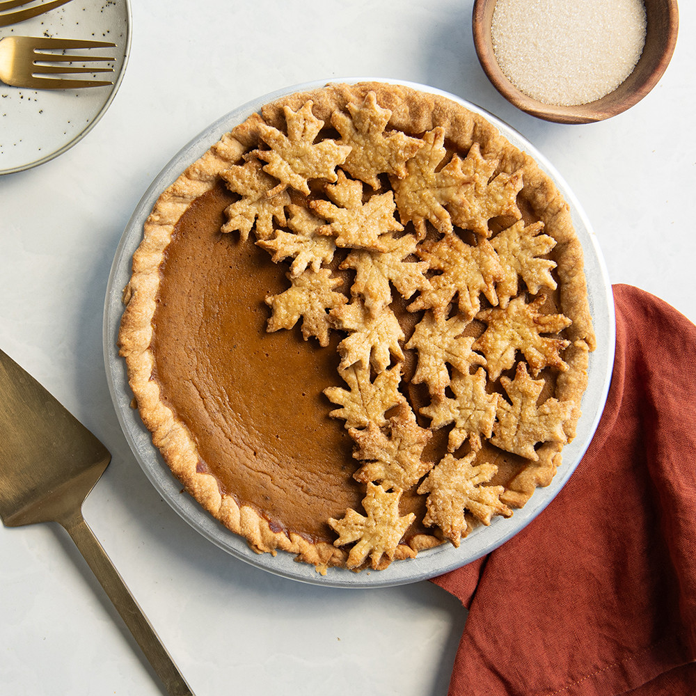 Golden pumpkin pie with decorative leaf-shaped crust cutouts arranged on top, baked in round pie pan