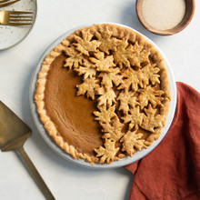 Golden pumpkin pie with decorative leaf-shaped crust cutouts arranged on top, baked in round pie pan