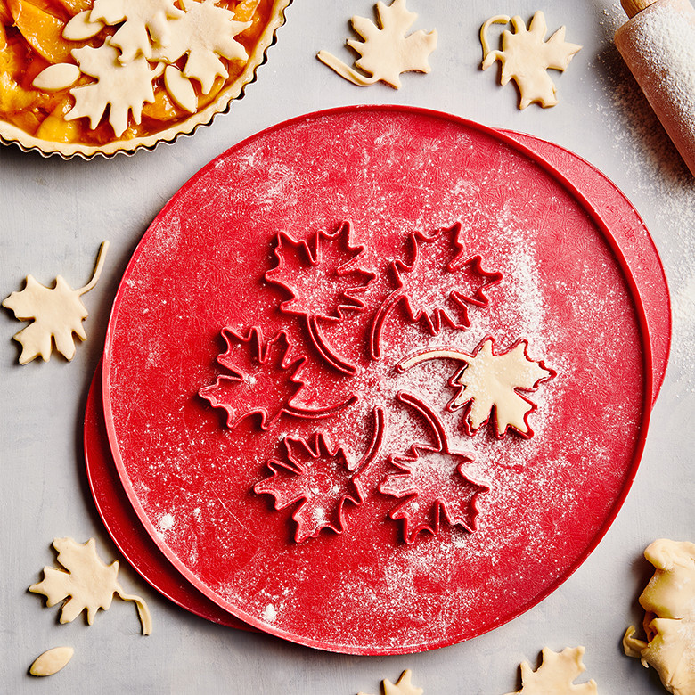Nordic Ware aluminum pie top cutter with leaf-shaped cutouts, dusted with flour alongside cut pastry leaves