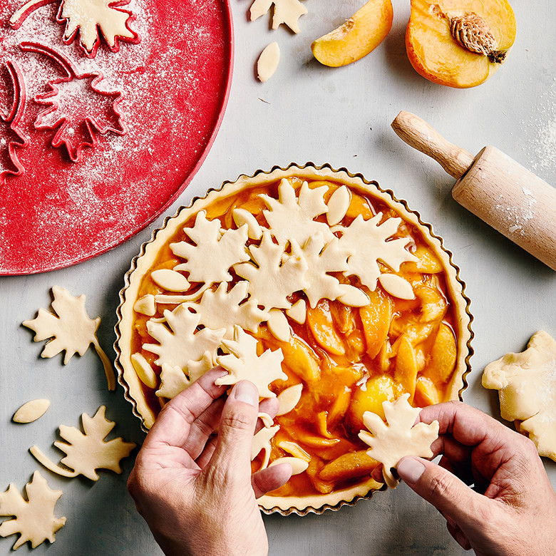 Hand placing Nordic Ware leaf-shaped pie cutter cutouts onto golden peach pie surface