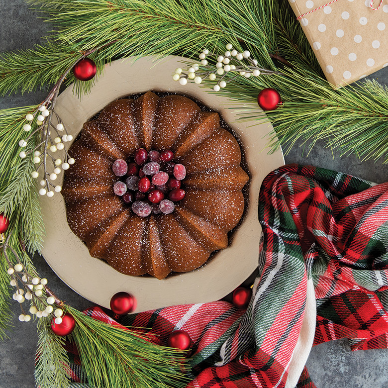 Golden bundt cake baked in fluted Nordic Ware Anniversary pan with holiday greenery and wrapped gift