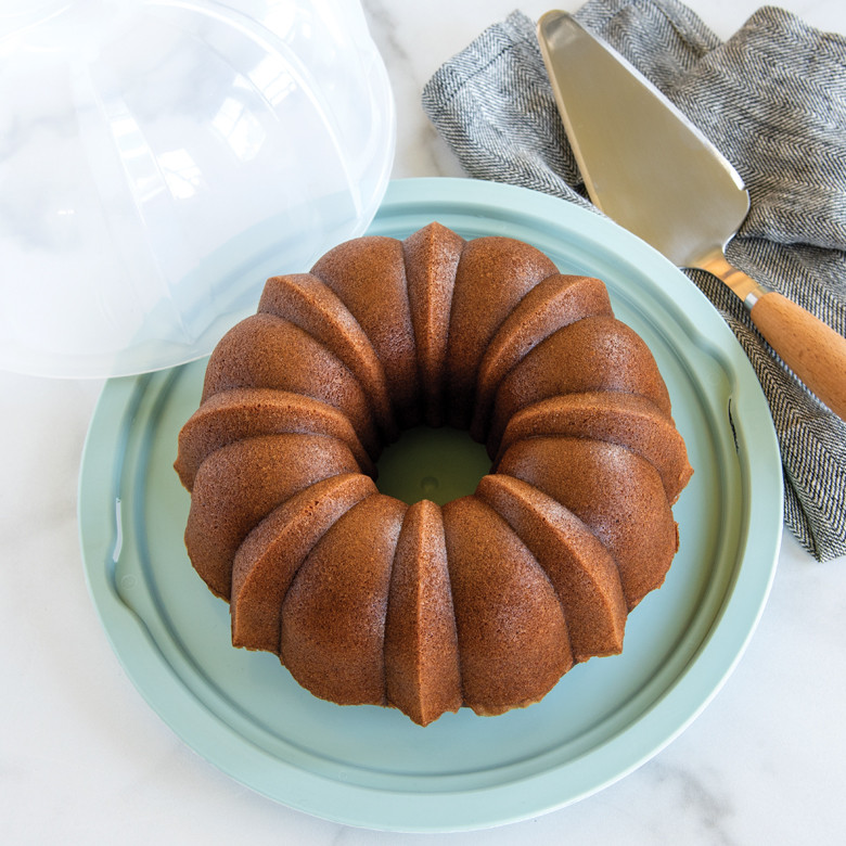 Clear plastic bundt cake keeper with domed lid containing golden baked bundt cake with fluted ridges