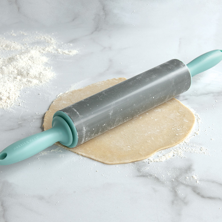 Nordic Ware nonstick rolling pin with black handles on floured surface beside rolled pie dough