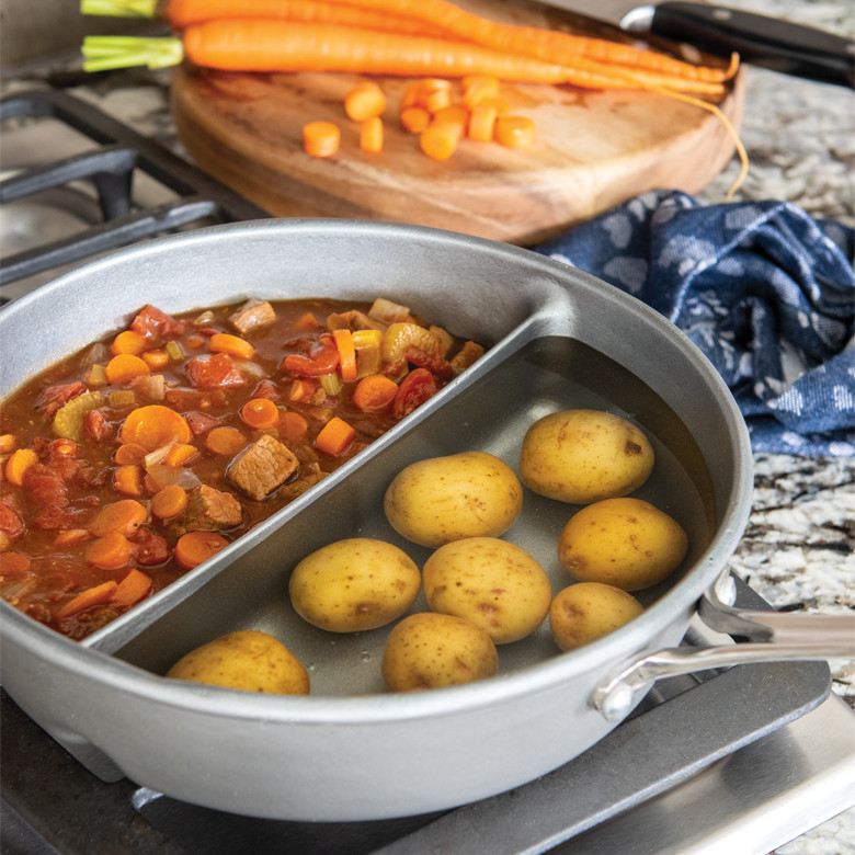 Nordic Ware aluminum divided saucepan on stovetop with boiling diced potatoes in one section and brown stew in other