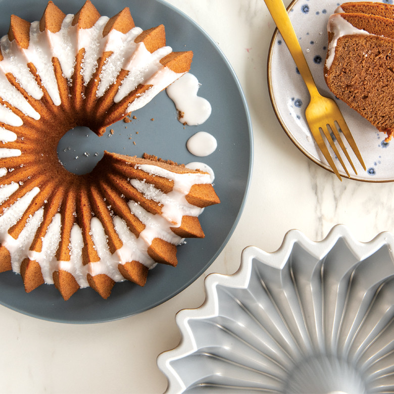 Golden spice bundt cake with white glaze next to Nordic Ware Brilliance bundt pan, slice cut on plate
