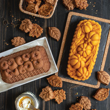 Sliced apple loaf cake, whole pumpkin wheat loaf, and decorative leaf-shaped baked goods arranged together
