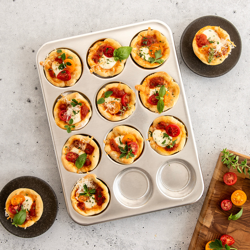 Nordic Ware aluminum 12-cup muffin pan with golden-brown pizza muffin bites, natural silver finish