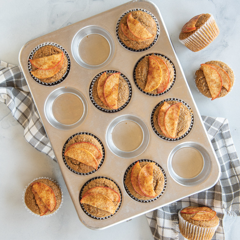 Twelve golden cinnamon muffins with apple slice garnish in Nordic Ware aluminum muffin pan, natural finish