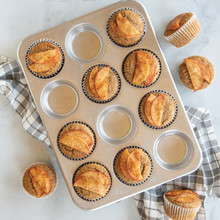 Twelve golden cinnamon muffins with apple slice garnish in Nordic Ware aluminum muffin pan, natural finish