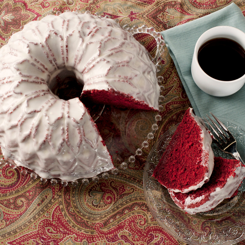Red velvet bundt cake with white glaze from Nordic Ware Stained Glass pan, showing geometric pattern, served slices with coffee
