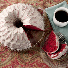 Red velvet bundt cake with white glaze from Nordic Ware Stained Glass pan, showing geometric pattern, served slices with coffee