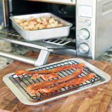 Nordic Ware aluminum baking set: rectangular casserole dish with cooked food in toaster oven, sheet pan with crispy bacon on cooling rack