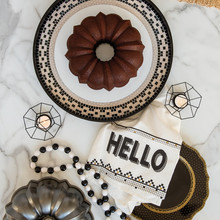 Chocolate bundt cake on white plate with Nordic Ware aluminum ProCast bundt pan in background