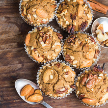 Six golden-brown muffins baked in Nordic Ware muffin pan on wooden surface with scattered nuts