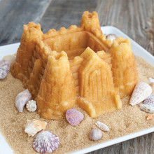Golden castle-shaped bundt cake with turret details on brown sugar sand with seashell decorations