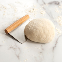 Nordic Ware stainless steel dough scraper positioned under mound of white flour dough on floured work surface