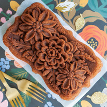 Baked wildflower-shaped loaf cake with two gold Nordic Ware cleaning forks on floral patterned surface