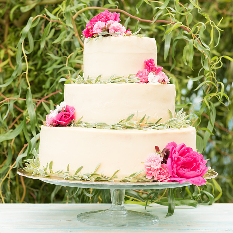 Three-tier white frosted wedding cake with pink roses and greenery, showcasing Nordic Ware round cake pans