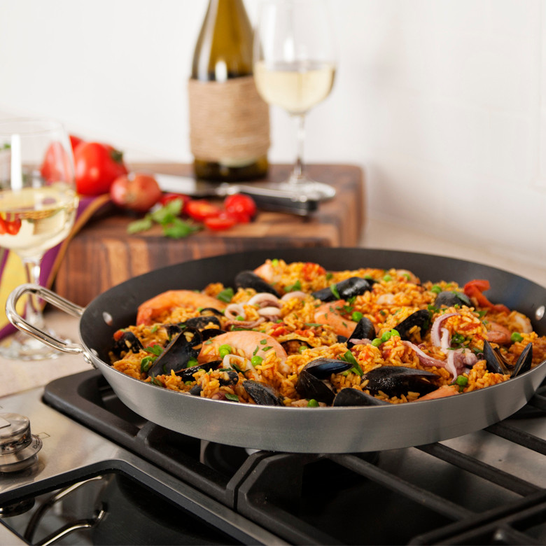 Nordic Ware paella pan with saffron rice, shrimp, mussels, and vegetables arranged on stovetop