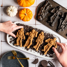 Spooky Skeleton Cakes on crumbled cookies, hands picking up cakes