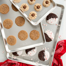 Nordic Ware aluminum baking sheet set with freshly baked holiday cookies including stars, snowflakes, and gingerbread shapes