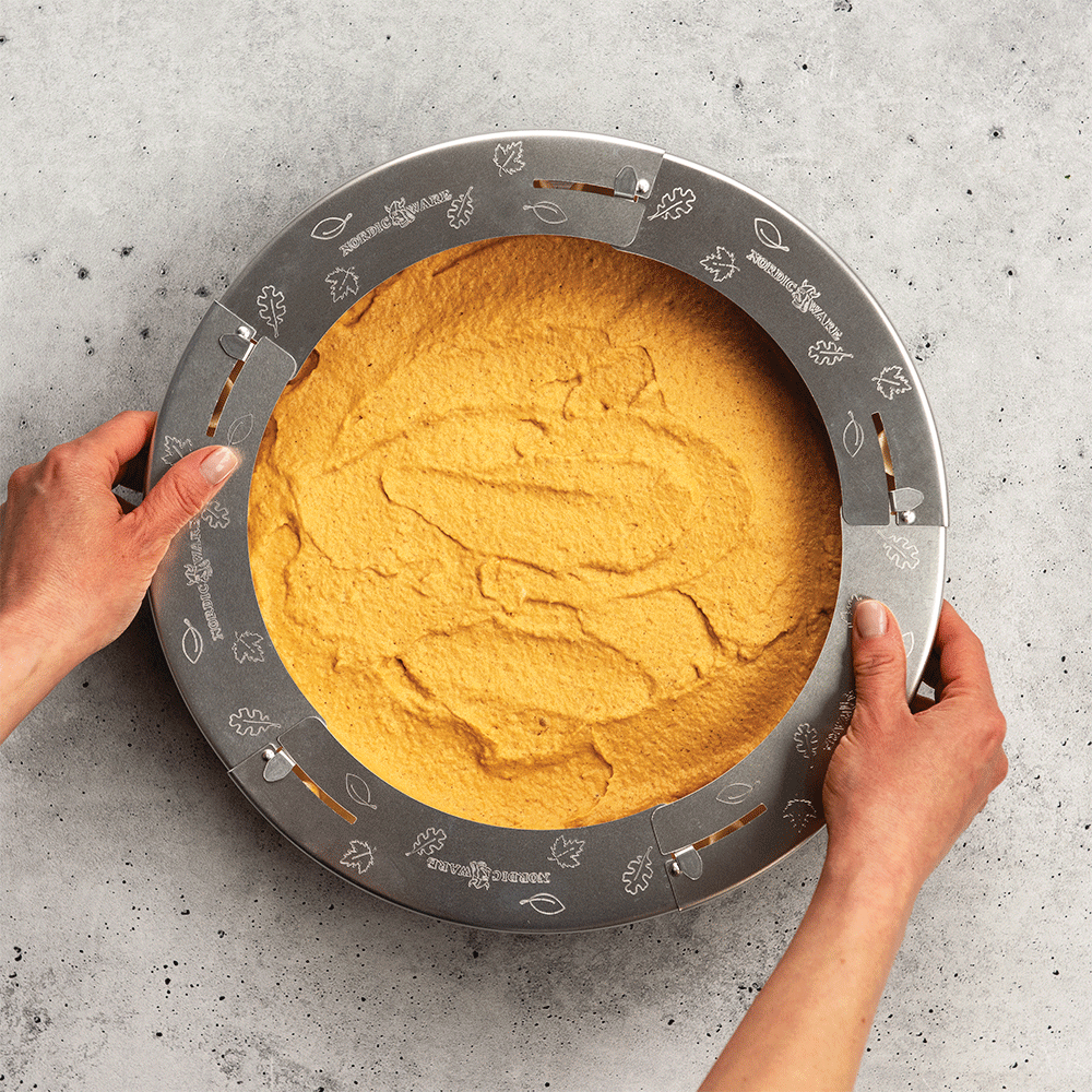 Nordic Ware aluminum adjustable pie crust shield being placed around golden pumpkin pie, demonstrating protective coverage