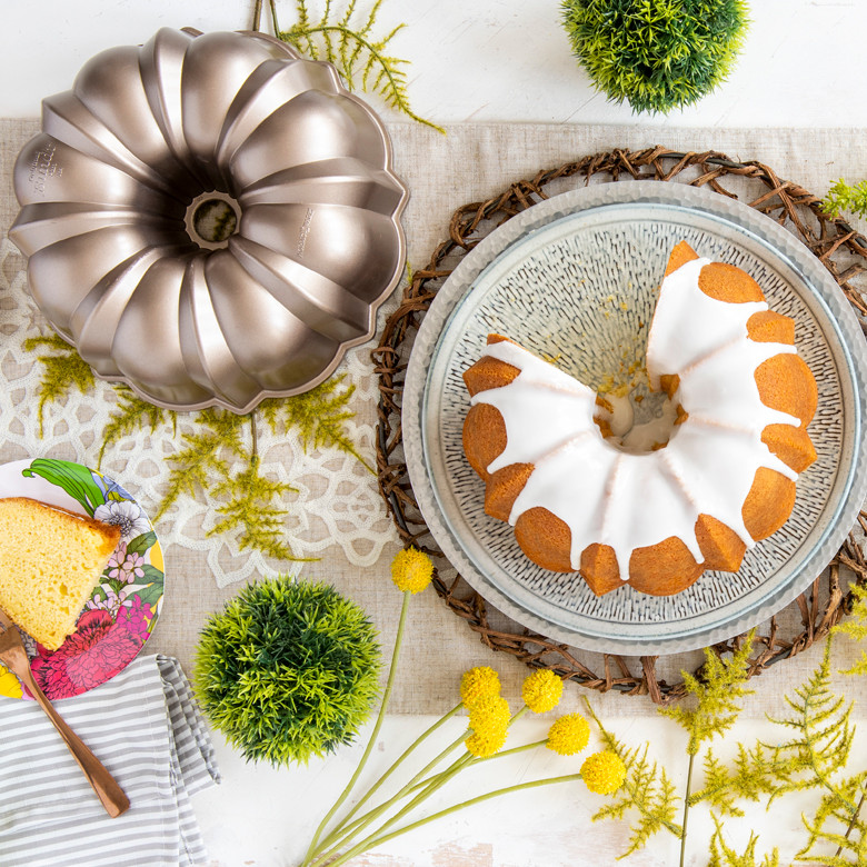 Golden bundt cake with white glaze on platter next to Nordic Ware toffee-colored bundt pan and plated slice
