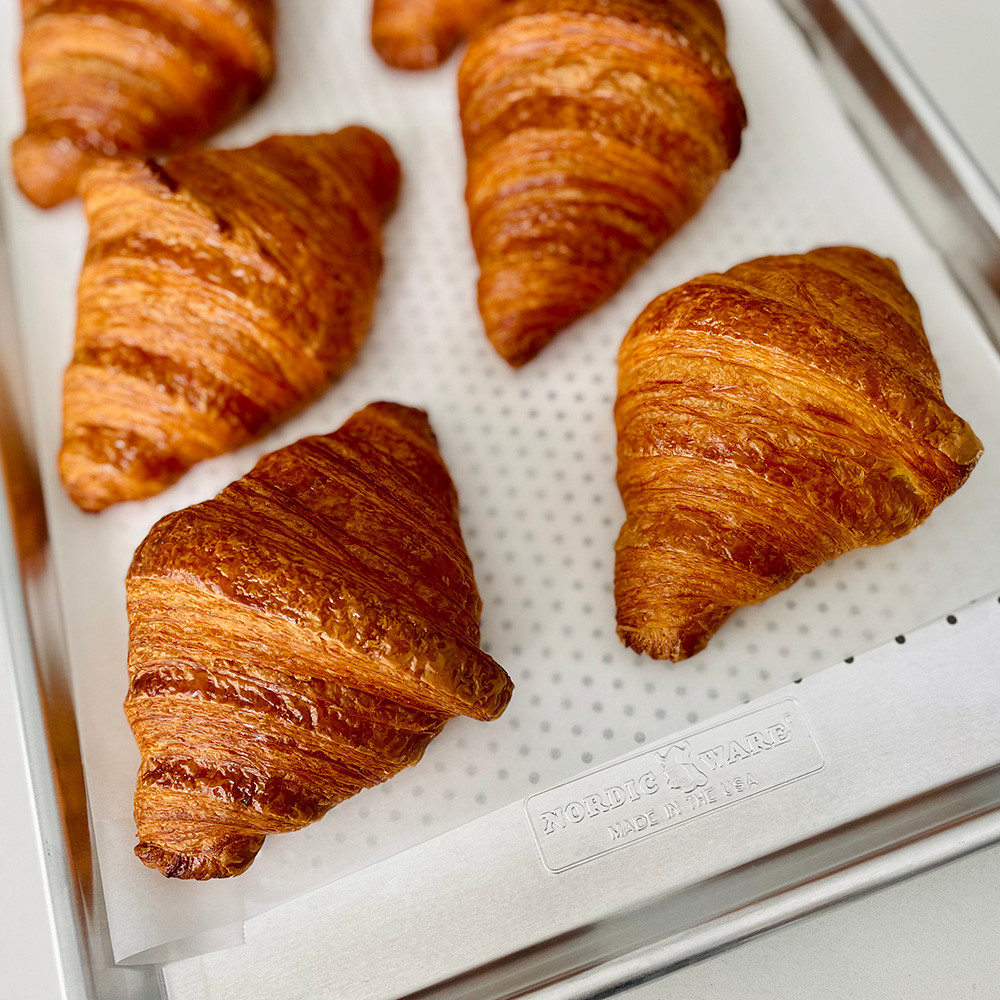 Golden baked croissants on Nordic Ware perforated aluminum half sheet pan with natural silver finish