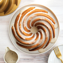 Golden glazed bundt cake on white plate beside Nordic Ware Heritage bundt pan showing detailed fluted pattern