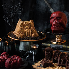 Halloween-themed bundt cakes and cakelettes on display stands with spooky decorations and carved pumpkins