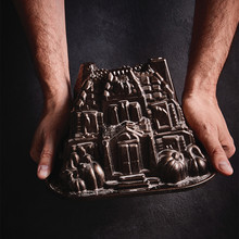 Two hands holding Nordic Ware Haunted Manor bundt pan, cast aluminum with intricate gothic architectural details