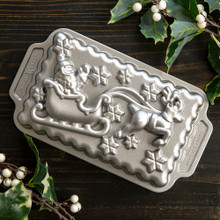 Nordic Ware aluminum Santa's sleigh loaf pan, detailed festive design, displayed with holiday candles and greenery