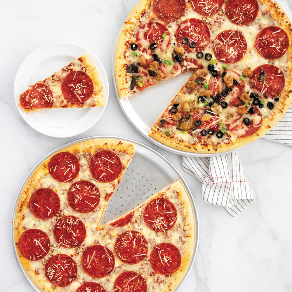 Two Nordic Ware aluminum pizza pans with baked pizzas - one traditional smooth, one perforated crisper pan