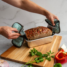 Hands lifting golden-brown glazed meatloaf using Nordic Ware aluminum pan with removable trivet handles