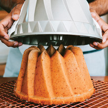 Hands lifting Nordic Ware Kugelhopf bundt pan revealing golden baked cake with distinctive fluted ridges