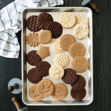 Nordic Ware Prism half sheet pan with assorted baked cookies in chocolate and vanilla, textured patterns