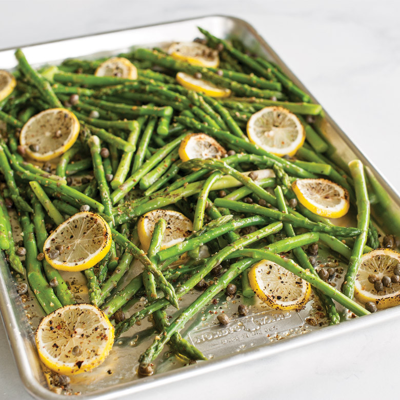 Roasted asparagus spears with lemon slices on Nordic Ware aluminum sheet pan, golden-brown and seasoned