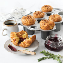 Golden-brown popovers in Nordic Ware six-cup popover pan with one plated beside jam and coffee