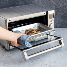 Hand removing Nordic Ware aluminum eighth sheet pan with baked chocolate chip cookies from toaster oven