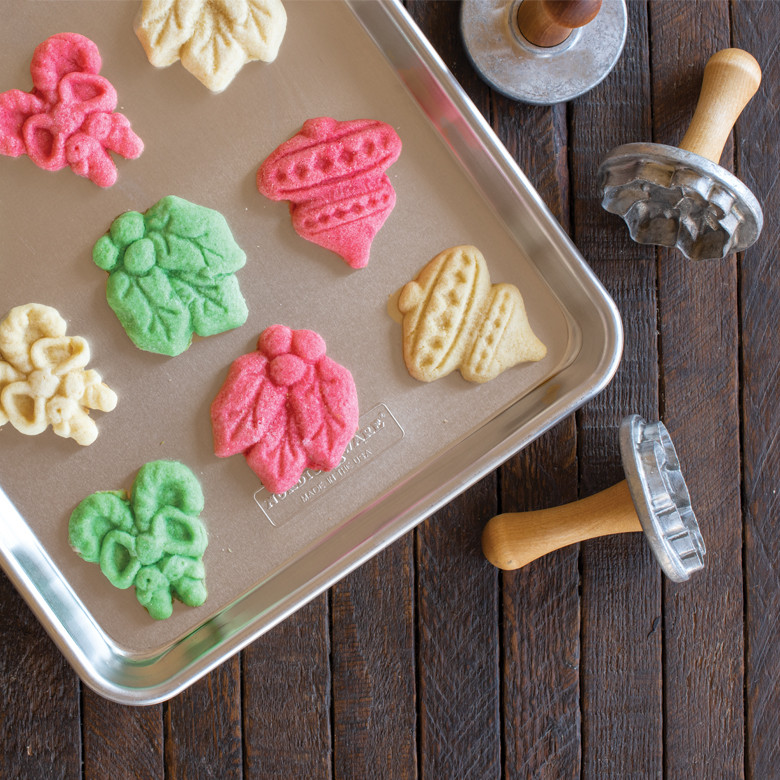 Nordic Ware aluminum baking sheet with colorful stamped sugar cookies in leaf, acorn, and tree shapes