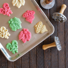 Nordic Ware aluminum baking sheet with colorful stamped sugar cookies in leaf, acorn, and tree shapes
