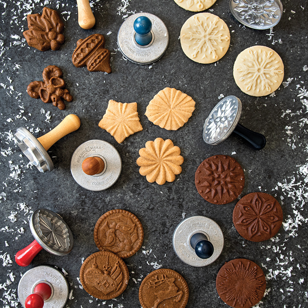 Holiday cookie stamps with baked cookies showing embossed winter designs, arranged on floured dark surface
