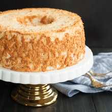 Golden angel food cake with fluffy texture and center hole on white ceramic cake stand with metallic base