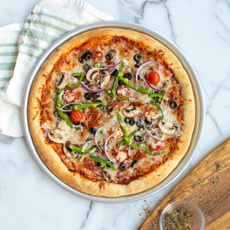 Baked vegetable pizza with olives, peppers, and red onions in Nordic Ware aluminum pizza pan with golden crust