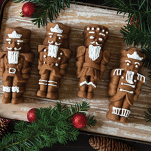 Four spice nutcracker cakelets with white icing details arranged on wooden board, decorated with pine and red ornaments