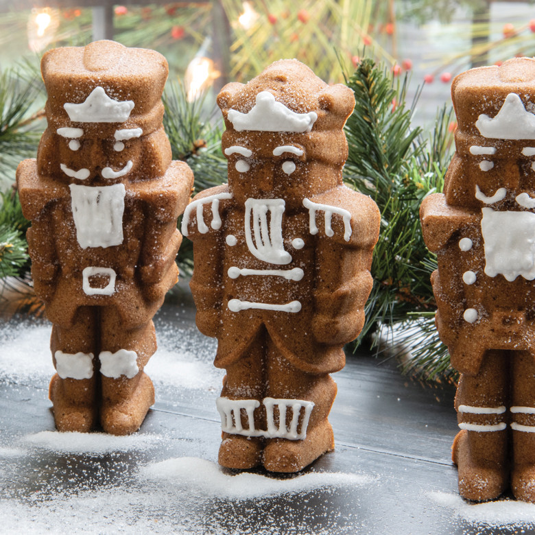 Baked spice nutcracker cakelets with white icing details and powdered sugar snow, evergreen sprigs in background