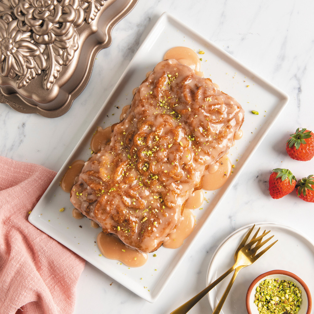 Frosted Wildflower loaf cake on rectangular plate with pan, strawberries, and pasticcios in a small dish 