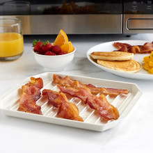 Nordic Ware white microwave bacon rack with crispy cooked bacon strips, surrounded by breakfast spread