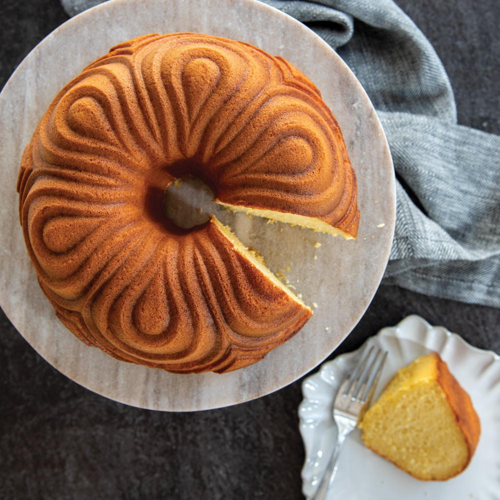 Golden brown chiffon bundt cake with decorative swirled ridges on white cake stand, baked in Nordic Ware pan