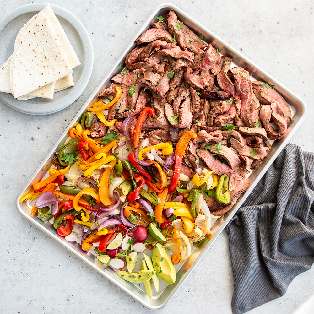 Nordic Ware aluminum sheet pan with sliced steak and colorful sautéed peppers and onions